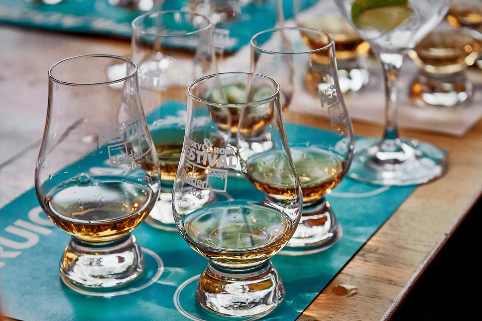 Række af klassiske whiskyglas med gylden spiritus opstillet til en organiseret smagning på en blå dug.