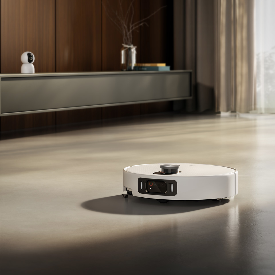 En hvid Xiaomi Robotstøvsuger 5 Pro navigerer hen over et gulv i en moderne stue med sollys.